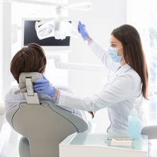 Female dentist doctor greeting patient sitting in dentist chair, turning lamp on, copy space