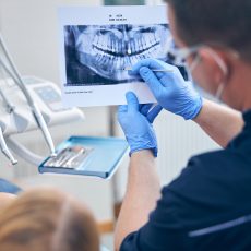 Male dentist is holding photo of woman teeth and explaining problems before starting treatment in office